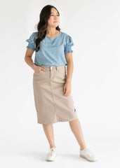 Woman wearing a blue polka dot top and beige skirt on a white background