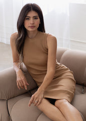 Woman in a beige dress sitting on a couch with a neutral background