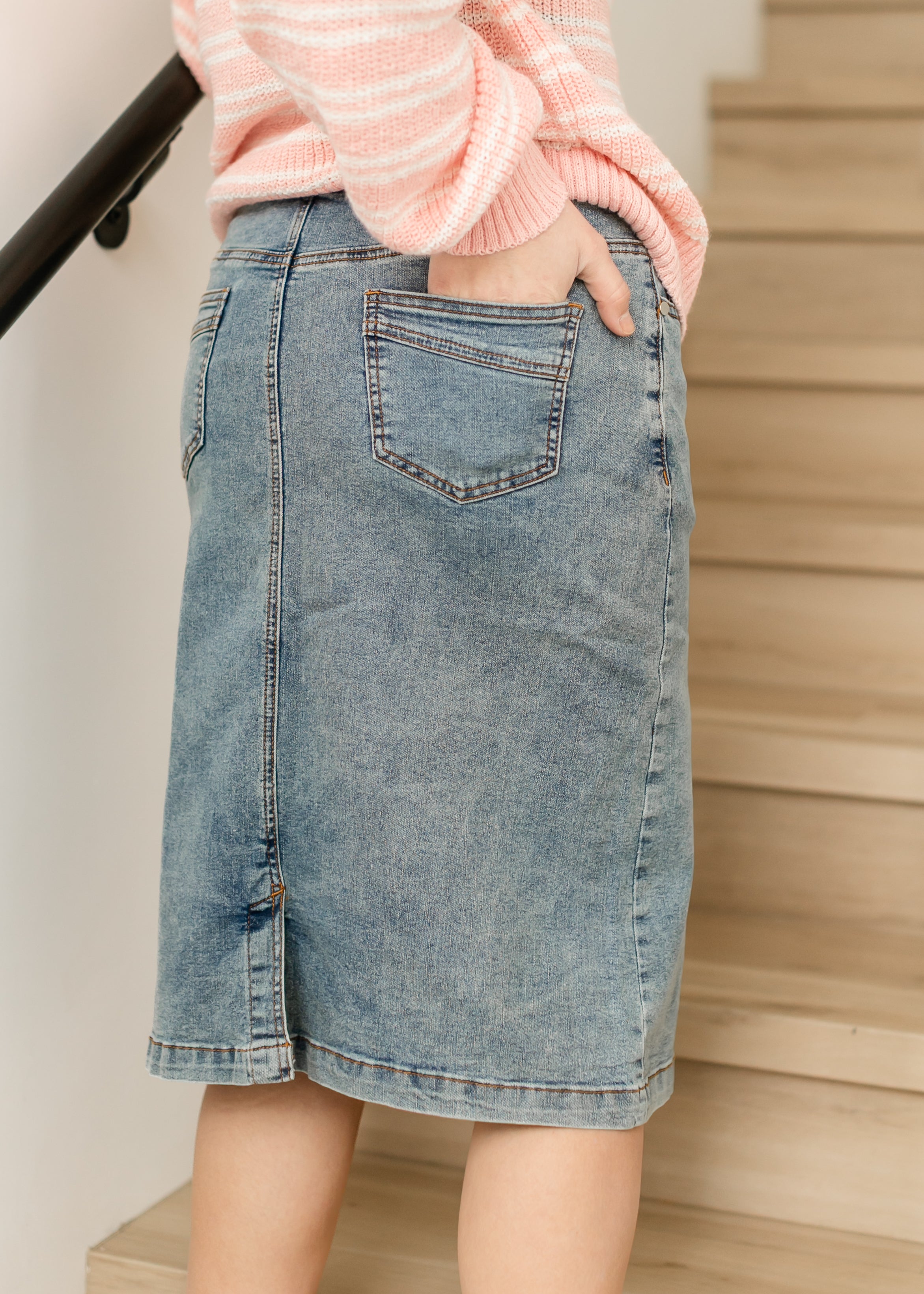 Person wearing a pink sweater and denim skirt standing on a staircase.