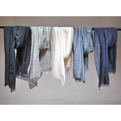 Set of five scarves in various shades of blue and gray hanging on a rod against a plain background.