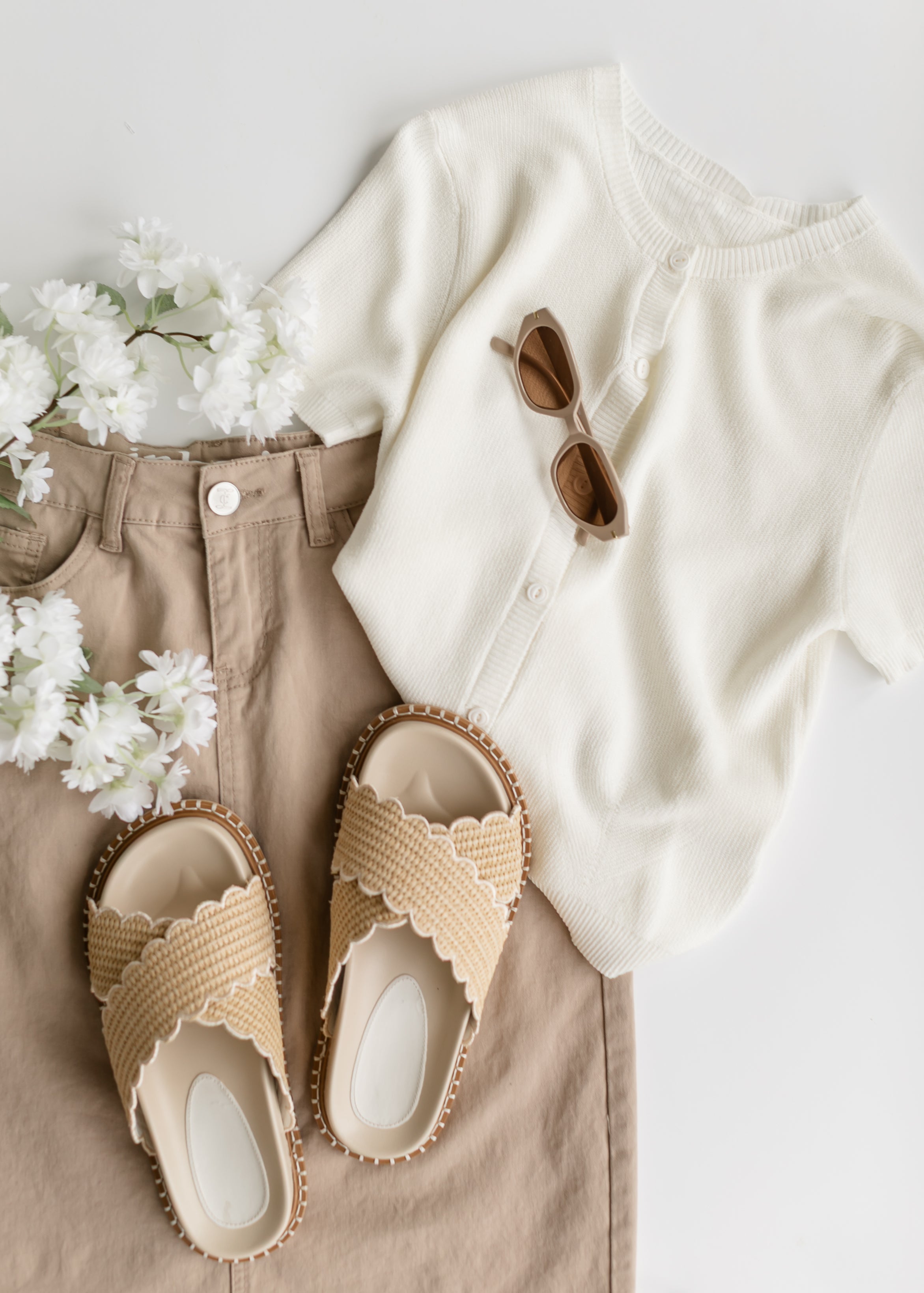 Beige sandals, white shirt, beige pants, and sunglasses on a light background
