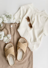 Beige sandals, white shirt, beige pants, and sunglasses on a light background