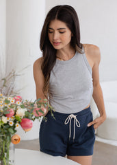 Woman wearing a gray tank top and navy shorts holding flowers indoors.