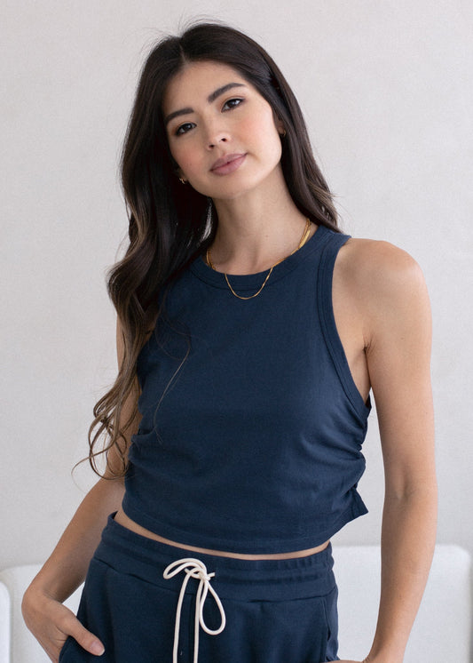 Woman wearing a navy blue sleeveless top and dark pants against a white background
