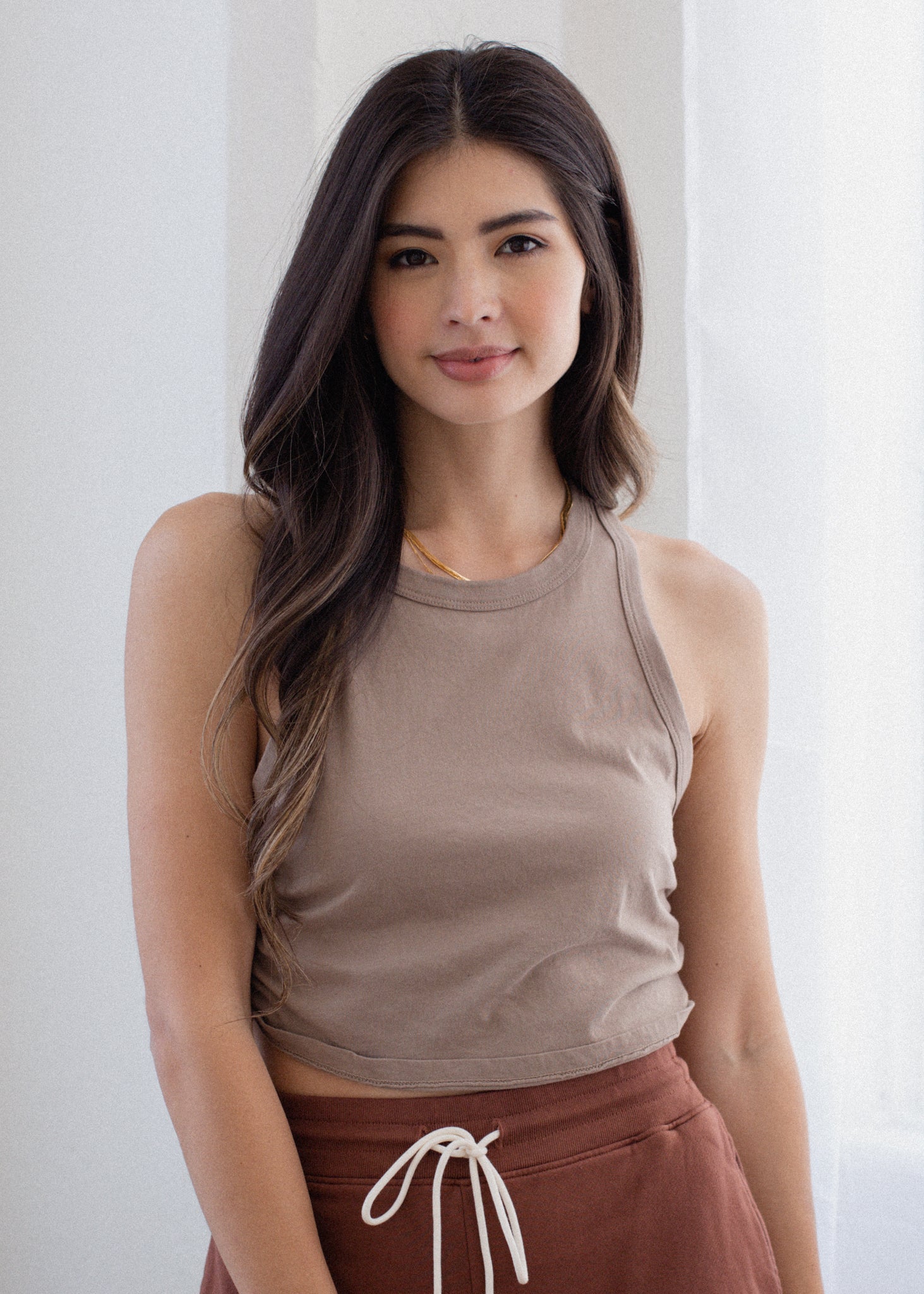 Woman wearing a brown tank top and maroon pants with a white background