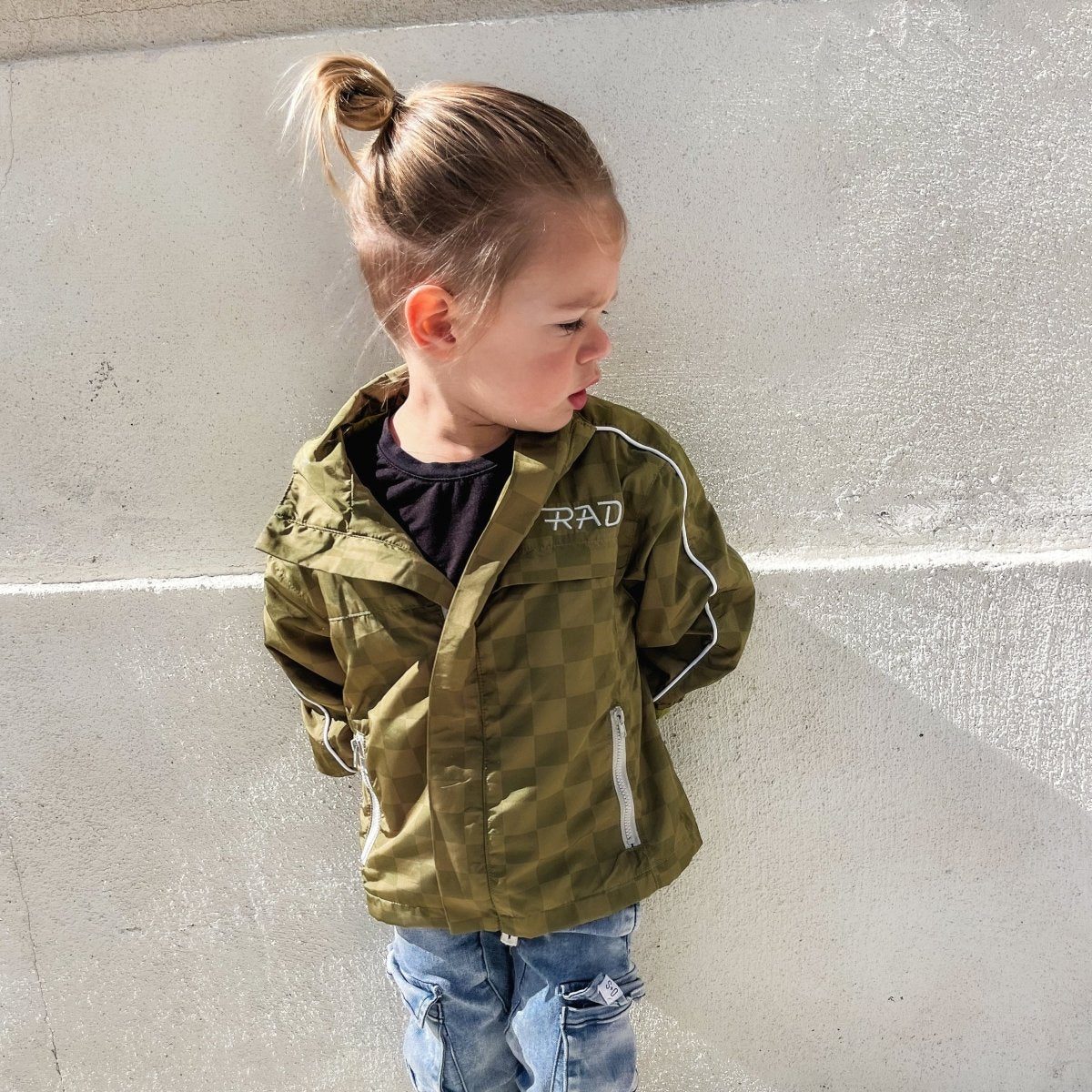 Child wearing a green jacket with 'RAD' branding against a gray wall