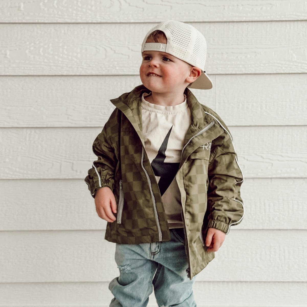 Child wearing a green jacket and white cap against a light background