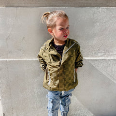 Child wearing a green jacket standing against a gray wall