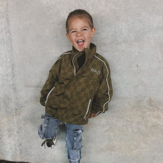 Child wearing a green jacket with 'RAD' logo against a gray concrete wall