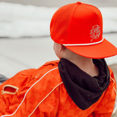 Person wearing an orange cap with 'Little Things' text and matching jacket outdoors.