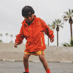 Child wearing an orange raincoat with palm trees in the background