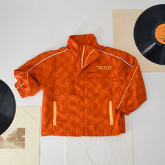 Orange jacket with 'RAD' logo on a white surface with vinyl records and a poster.