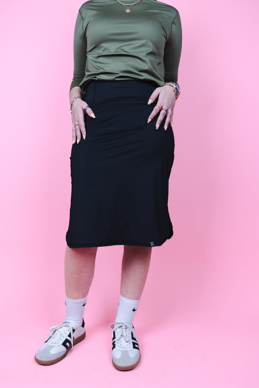Person wearing a green top and black skirt on a pink background