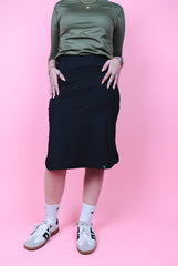 Person wearing a green top and black skirt on a pink background