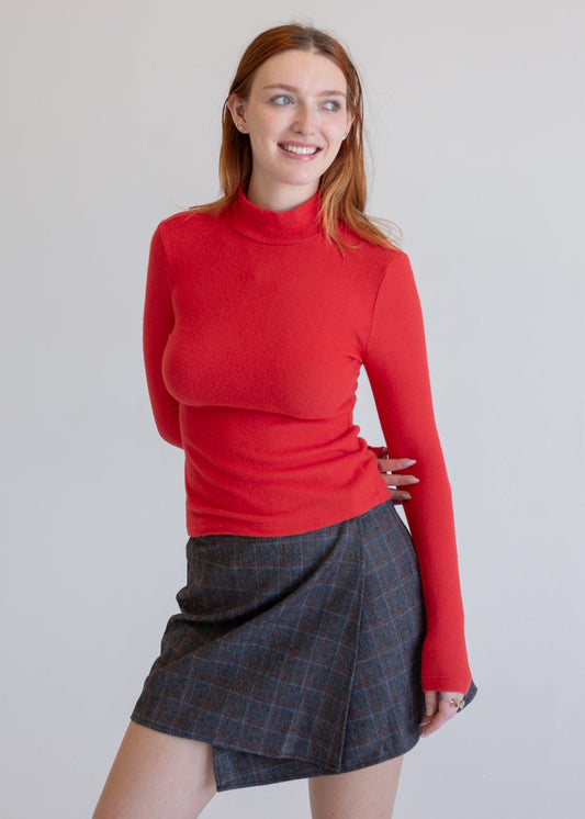 Woman wearing a red sweater and plaid skirt against a plain background