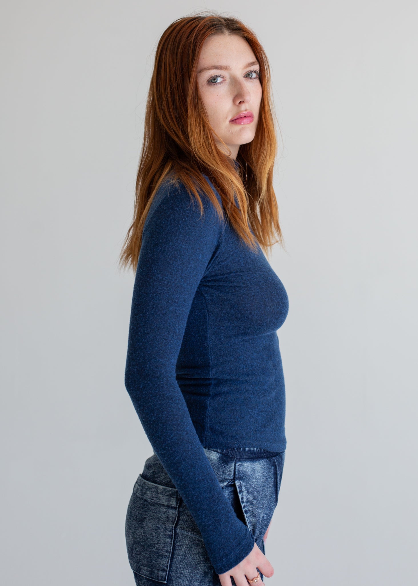 Woman wearing a blue long-sleeve top and jeans on a plain background