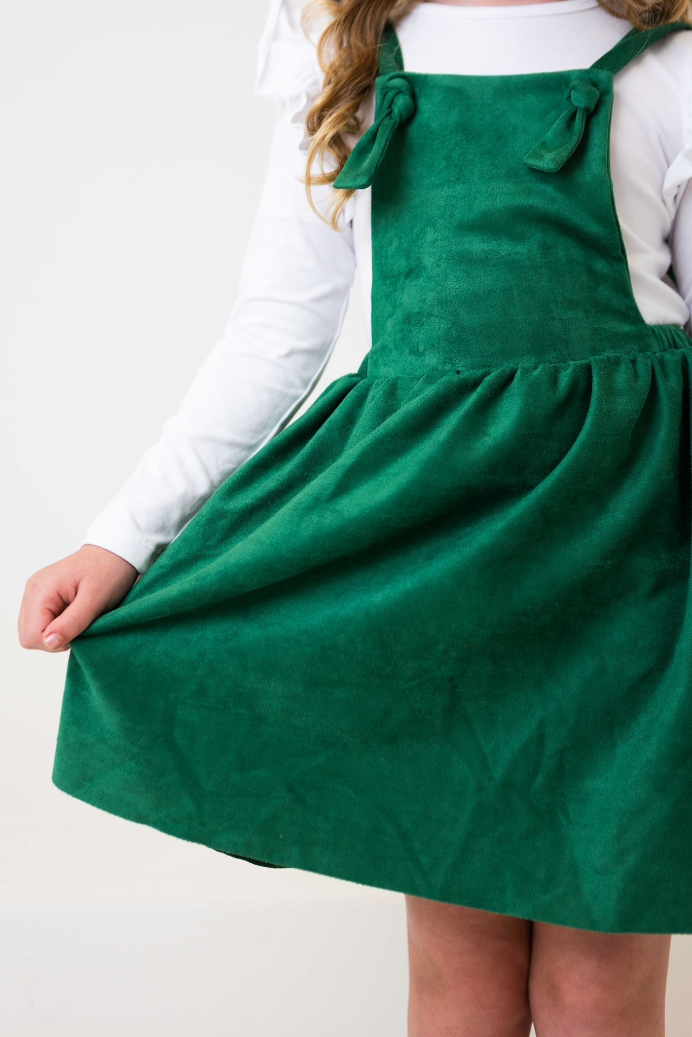 Green pinafore dress worn by a child on a white background