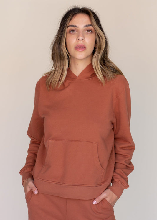 Woman wearing a brown hoodie against a beige background
