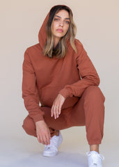 Woman wearing a brown hoodie and matching pants with white sneakers on a beige background