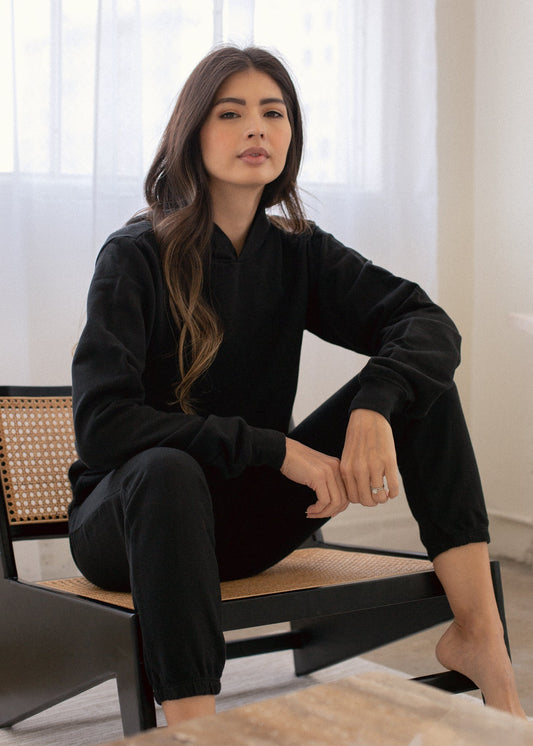 Woman in a black outfit sitting on a chair with a neutral background