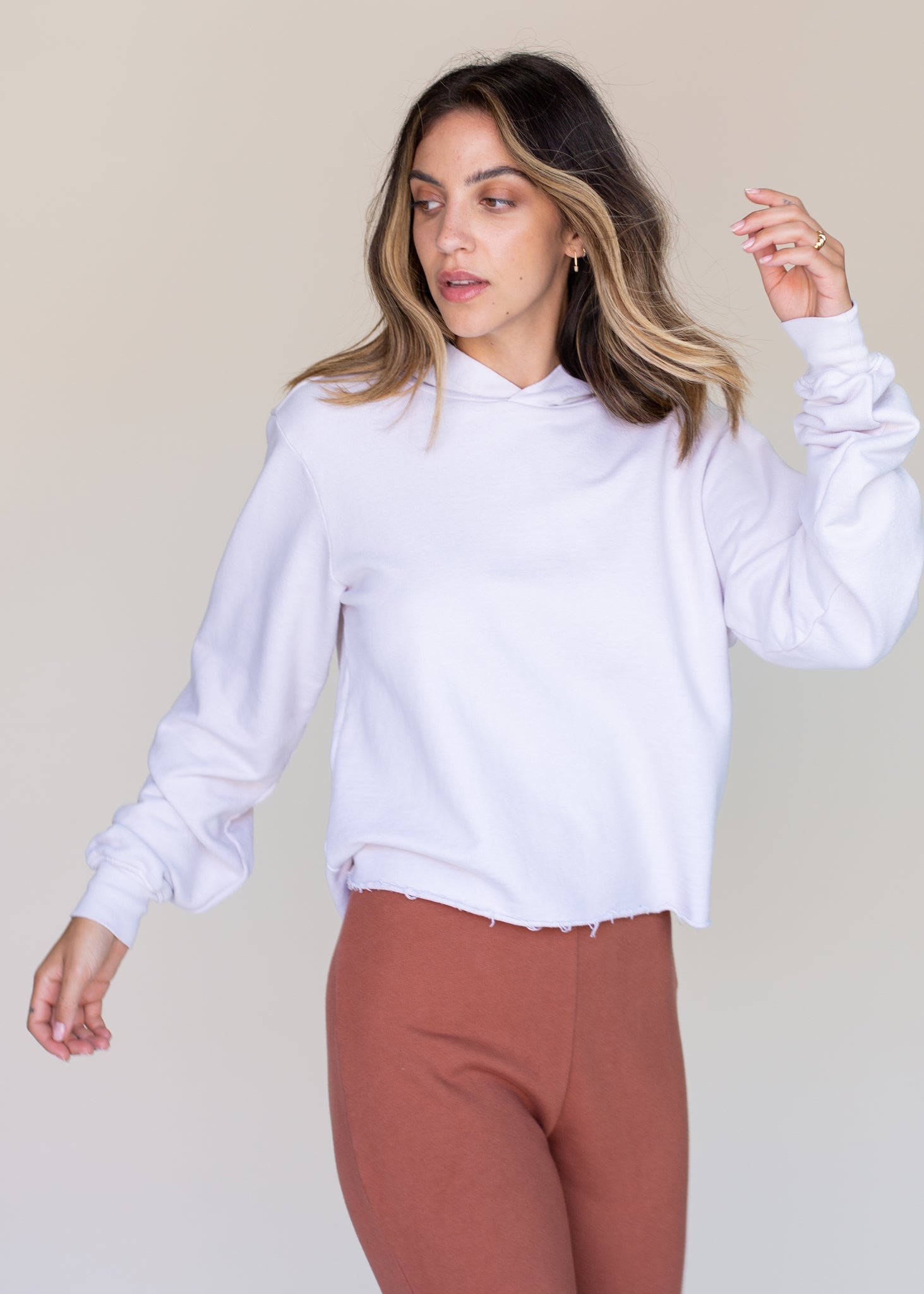 Woman wearing a white hoodie and brown pants against a beige background