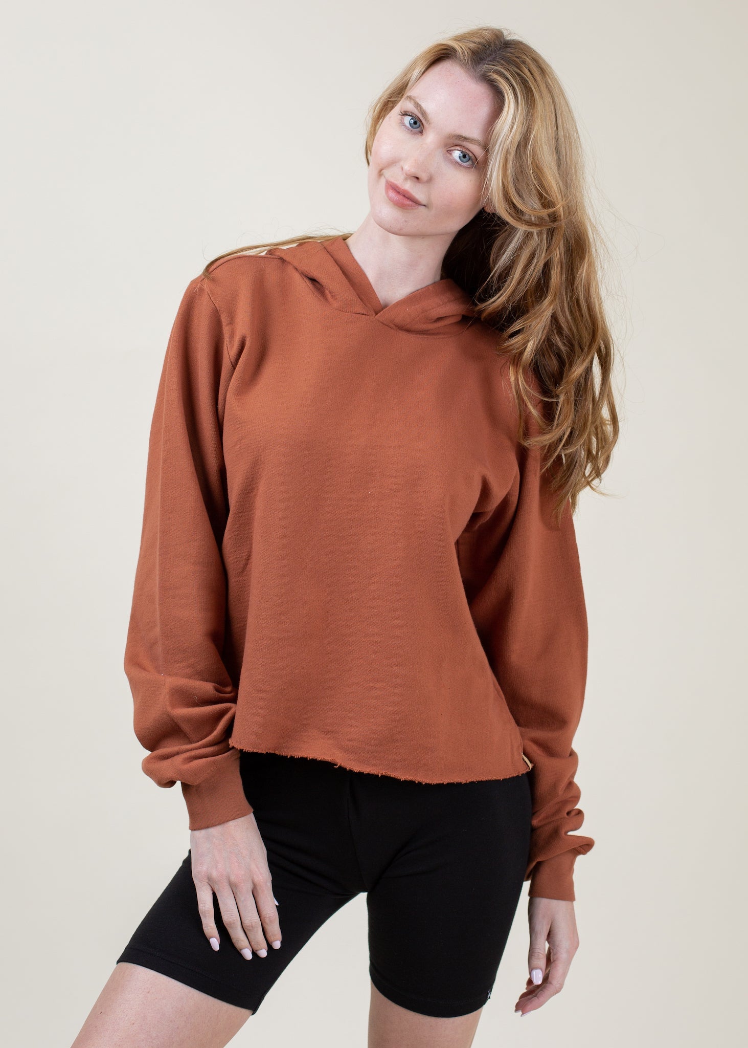 Woman wearing a brown hoodie and black shorts on a plain background