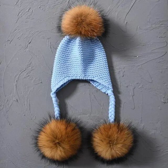 Blue knitted hat with brown fur pom-poms on a gray textured background