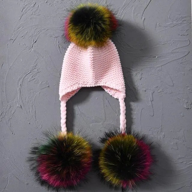 Pink knitted hat with colorful pom-poms on a gray textured background